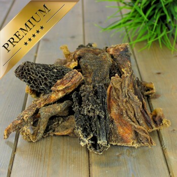 Hochwertige Hundeleckerlis aus verschiedenen getrockneten Fleischstücken, auf einer Holzoberfläche mit einer grünen Pflanze im Hintergrund präsentiert.