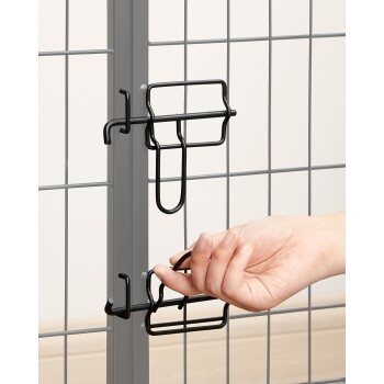 Eine Hand, die einen schwarzen Metallriegel an einem grauen Haustiergehege-Tor entriegelt, das den sicheren Verschlussmechanismus zeigt.
