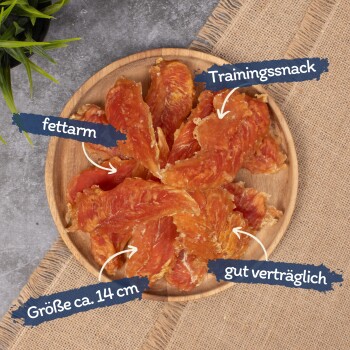 Getrocknete Hähnchenstreifen auf einem Holzbrett angeordnet, beschriftet als "Trainingssnack," "fettarm," "Größe ca. 14 cm," und "gut verträglich."