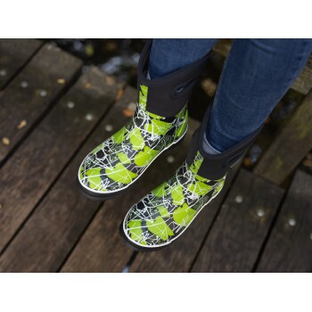 Ein Paar lebhaft grüne und schwarz gemusterte Gummistiefel, die von einer Person auf einer Holzterrasse getragen werden.