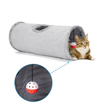 Eine getigerte Katze, die in einem weichen grauen Tunnel liegt, mit einem hängenden rot-weißen Ballspielzeug darin.