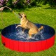 Ein glücklicher Hund planscht in einem rot-blauen Haustierpool, während Wasser aus einem Schlauch spritzt, den eine Person hält, auf grünem Gras.