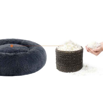 Rundes dunkelgraues Plüsch-Donut-Haustierbett neben einem geflochtenen Korb mit weißer Füllung, Hände halten die Füllung