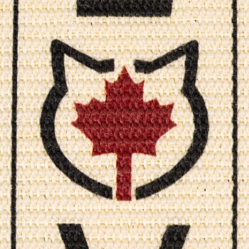 Nahaufnahme eines gewebten Stoffes mit einer schwarzen Umrisslinie eines Katzenkopfes und einem roten Ahornblatt in der Mitte.