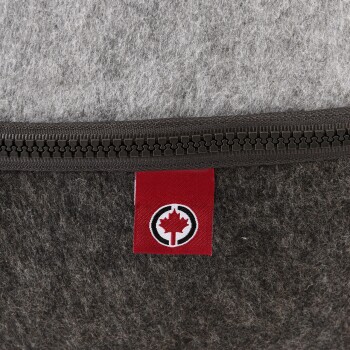 Nahaufnahme eines Haustierbettes mit grauem und dunkelbraunem Filzmaterial, mit einem roten Etikett, das ein Ahornblatt-Logo und einen Reißverschluss zeigt.