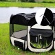 Ein tragbarer Tierspielplatz in Schwarz und Creme mit Netzseiten auf Gras am Wasser, mit einem 15 cm hohen Anpassungsbereich.
