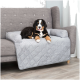 Ein flauschiger Bernersennenhund-Welpe liegt auf einem grauen, gesteppten Sofabezug und ruht auf einem grauen Sofa mit Knopfdetails.