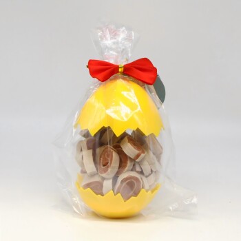 Klarer Plastikbeutel mit gelbem, zerbrochenem eiförmigem Behälter gefüllt mit runden Hundeleckerlis, mit roter Schleife gebunden.