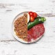 Ein geteilter Teller mit Haustierfutter auf der linken Seite und frischen Zutaten auf der rechten Seite: rohes Steak, Zucchini, Kirschtomaten und ein Apfelschnitz.
