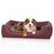 Ein glücklicher Australian Shepherd Hund entspannt sich in einem burgunderfarbenen Haustierbett mit weißem Rand, mit einem Holzschild, auf dem "KNUDDELWUFF" steht.