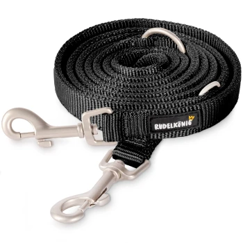 Schwarze Hundeleine mit silbernen Metallclips und einem Markenetikett mit der Aufschrift "RUDELKÜNIG", ordentlich auf einem weißen Hintergrund aufgerollt.