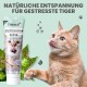 Eine verspielte orangefarbene Katze leckt sich die Lippen neben einer Tube 'noms+ Wohlfühlpaste' für gestresste Katzen, mit Text, der natürliche Entspannung fördert.