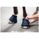 Eine Person passt einen blauen Hufschuh am Vorderbein eines Pferdes an, wobei das weiche Futter und das Logo des Schuhs gezeigt werden.