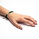 Eine Hand mit einem grünen Perlenarmband, das eine weiße Perle mit einem schwarzen Pfotenabdruck zeigt, ruht auf einer weißen Oberfläche.