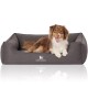 Ein glücklicher braun-weißer Hund, der auf einem grauen Hundebett mit erhöhtem Rand liegt, mit dem Logo "KNUFFELWUFF."