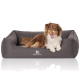Ein glücklicher braun-weißer Hund, der auf einem grauen Hundebett mit erhöhtem Rand liegt, mit dem Logo "KNUFFELWUFF."