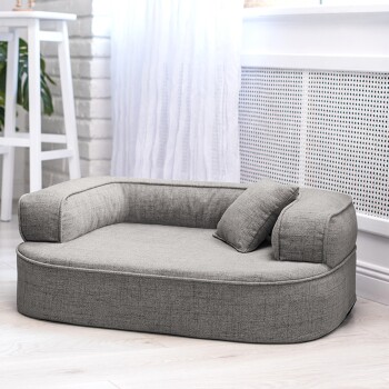 Ein schwarz-brauner Dackel steht auf einem plüschigen grauen Haustierbett mit einem kleinen Kissen, vor einem hellen Holzboden.