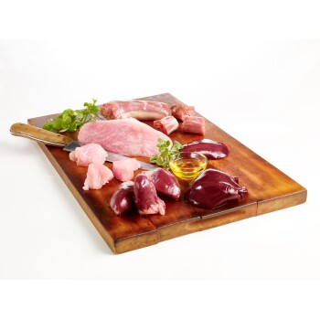 Rohe Fleisch- und Organstücke auf einem Holzschneidebrett angeordnet, einschließlich Hühnerleber, Schweinefleisch und einer kleinen Schüssel mit Öl.