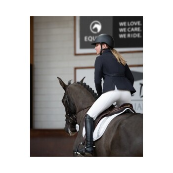 Ein Reiter in einer schwarzen Jacke und einem Helm sitzt auf einem grauen Pferd, trägt weiße Reithosen und hohe schwarze Stiefel in einer Reithalle.