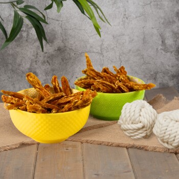 Zwei Schalen gefüllt mit Haustierleckereien, eine gelbe und eine grüne, stehen auf einer Holzoberfläche neben zwei weißen Seilspielzeugen.