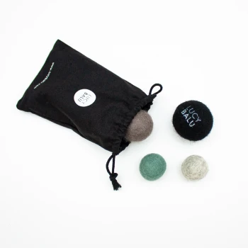 Eine schwarze Zugtasche mit der Aufschrift "Lucy Balu" enthält drei bunte Filzkugeln in Grau, Grün und Schwarz, wobei eine Kugel den Markennamen trägt.