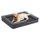 Gelber Labrador mit orangefarbener Halsbinde auf grauem Hundebett mit erhöhtem Rand und kleinem Markenetikett vorne (Text nicht lesbar).