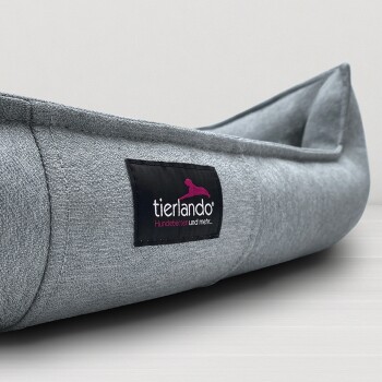 Graues Stoff-Hundebett mit einem schwarzen Etikett mit der Aufschrift „tierlando Hundebetten und mehr...“ auf einer hellen Oberfläche.