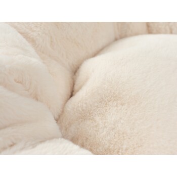 Nahaufnahme eines weichen, plüschigen Haustierbettes in einer cremigen beige Farbe, das seine flauschige Textur und einladenden Komfort zeigt.