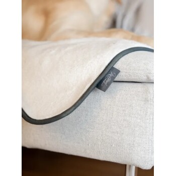 Nahaufnahme einer beigen Haustierdecke mit dunklem Rand und einem "FurPaw"-Etikett an einer hellgrauen Sofaecke.