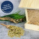 Holz-Vogelfutterspender mit grünem Vogelfutter in einer Schaufel, umgeben von Gras und Treibholz; Text: "Ideal als Vogelfutter-Ergänzung."