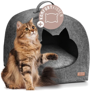 Langhaarterrier/Langhaarkatze (getigert) mit erhobener Pfote neben grauem Filz-Katzenhöhlenbett mit katzenohrförmiger Öffnung und Schild 'KOMFORTKISSEN'