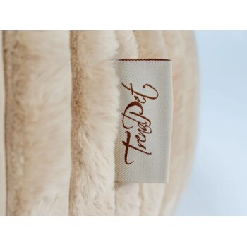 Nahaufnahme eines beigen Plüsch-Haustierbetts mit einem Stoffetikett, auf dem "TrendPet" in brauner Schrift steht.