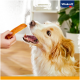 Ein Golden Retriever schaut gespannt zu einer Hand auf, die einen Hundesnack hält, mit einer gemütlichen Inneneinstellung im Hintergrund. Vitakraft-Logo sichtbar.