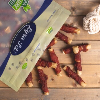 Eine Tüte mit Haustierleckerlis, die teilweise geöffnet ist und mehrere gerollte Leckerlis, die mit Fleisch überzogen sind, auf einer Holzoberfläche verstreut zeigt.