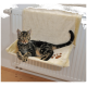 Eine getigerte Katze, die auf einem weichen, cremefarbenen Katzenbett sitzt, das an einem Heizkörper befestigt ist, mit einem Pfotenabdruckdesign, das an der Seite sichtbar ist.
