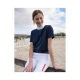Ein junger Reiter in einem marineblauen Reitshirt und weißen Reithosen sitzt auf einem Holzzaun in einer Pferdespringarena.