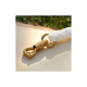 Nahaufnahme eines goldenen Metallclips, der an einer weißen geflochtenen Leine befestigt ist, auf einer hellen Holzoberfläche mit grünem Gras im Hintergrund.