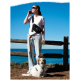 Eine Frau in einem weißen T-Shirt und Jeans hält ein Telefon und ein grünes Getränk an einem Zaun, mit einem glücklichen Hund an der Leine und dem Ozean im Hintergrund.