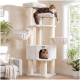 Cremefarbener Kratzbaum im Wohnzimmer mit drei Katzen: oberes Aussichtsbrett, Hängematte und Höhle (kleines Logo an der Höhle); Pflanzen und Fenster.