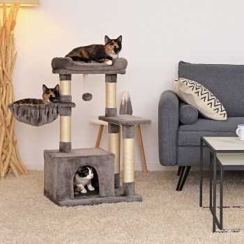 Ein gemütliches Wohnzimmer mit einem mehrstöckigen Katzenbaum und drei schildpattfarbenen Katzen: eine oben, eine in einem Korb und eine in einem Versteck.