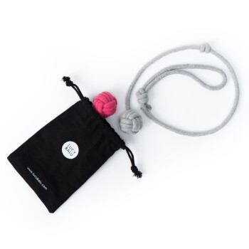 Ein schwarzer Beutel mit Kordelzug mit einem Logo, der zwei bunte Knoten-Spielzeuge (eins pink, eins grau) und ein graues Seilspielzeug enthält, auf einem weißen Hintergrund.
