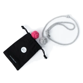 Ein schwarzer Beutel mit Kordelzug mit einem Logo, der zwei bunte Knoten-Spielzeuge (eins pink, eins grau) und ein graues Seilspielzeug enthält, auf einem weißen Hintergrund.