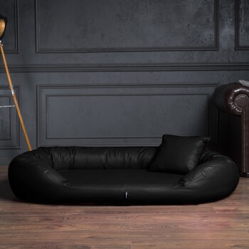 Schwarzes Leder-Haustierbett mit Kissen auf Holzboden vor dunkelgrauer vertäfelter Wand.