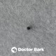 Nahaufnahme eines weichen grauen Haustierbettstoffs mit einem kleinen schwarzen Punkt, mit dem Logo "Doctor Bark" deutlich am unteren Rand.