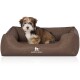Ein kleiner, flauschiger Hund sitzt bequem in einem stilvollen braunen Haustierbett mit einem gesteppten Innenraum, mit dem Logo "KNUFFELWUFF."