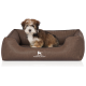Ein kleiner, flauschiger Hund sitzt bequem in einem stilvollen braunen Haustierbett mit einem gesteppten Innenraum, mit dem Logo "KNUFFELWUFF."