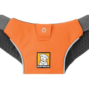 Nahaufnahme eines orangefarbenen Hundegeschirrs mit einem schwarzen und gelben 'Ruffwear'-Logo und einer Hundegrafik, entworfen für die Sicherheit von Haustieren.