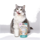Eine flauschige grau-weiße Katze leckt sich die Lippen neben einem Glas Milch und einem Beutel mit der Aufschrift 'Vitamin-Milchshake Entspannung' von CatLabs.