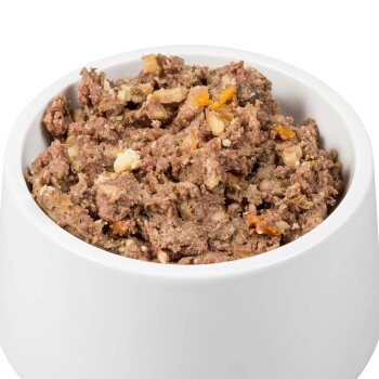 Eine weiße Haustierschüssel gefüllt mit einer stückigen, feuchten Mischung aus Fleisch und Gemüse, die eine Vielzahl von Texturen und Farben zeigt.