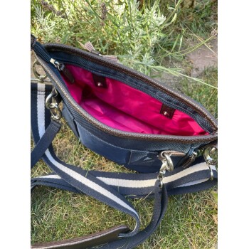 Eine Nahaufnahme einer marineblauen Haustiertragetasche mit pinkem Innenraum, mit einem gestreiften Riemen und einem Reißverschluss, die auf Gras ruht.